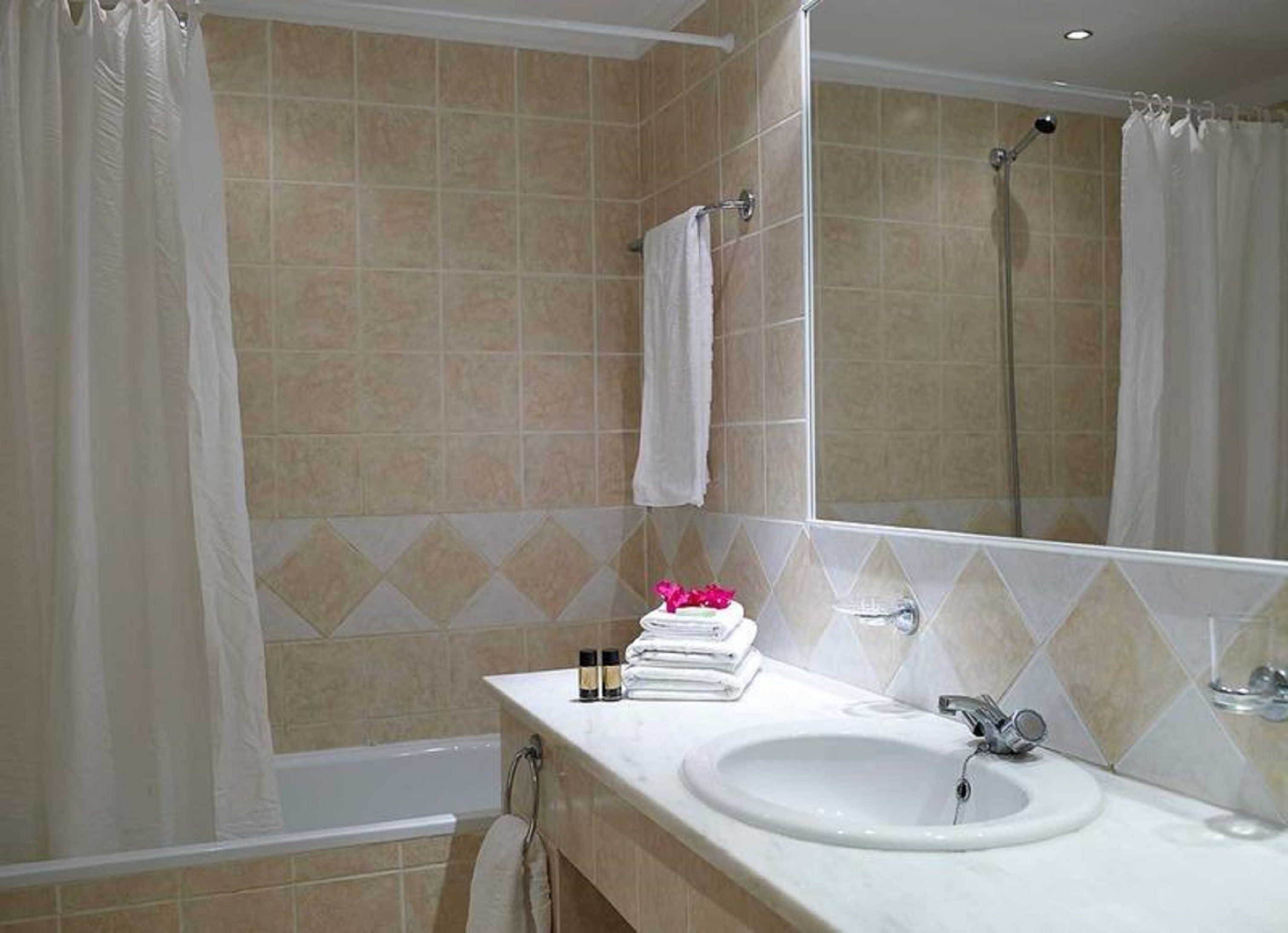 Ein Badezimmer mit beige gefliesten Wänden, einem weißen Waschbecken, einem Spiegel und einer Duschkabine.