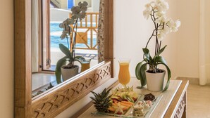 A breakfast tray with fruits and pastries, a glass of orange juice, and two potted orchids on a marble counter. - Canvas by Mitsis Family Village (Kos)