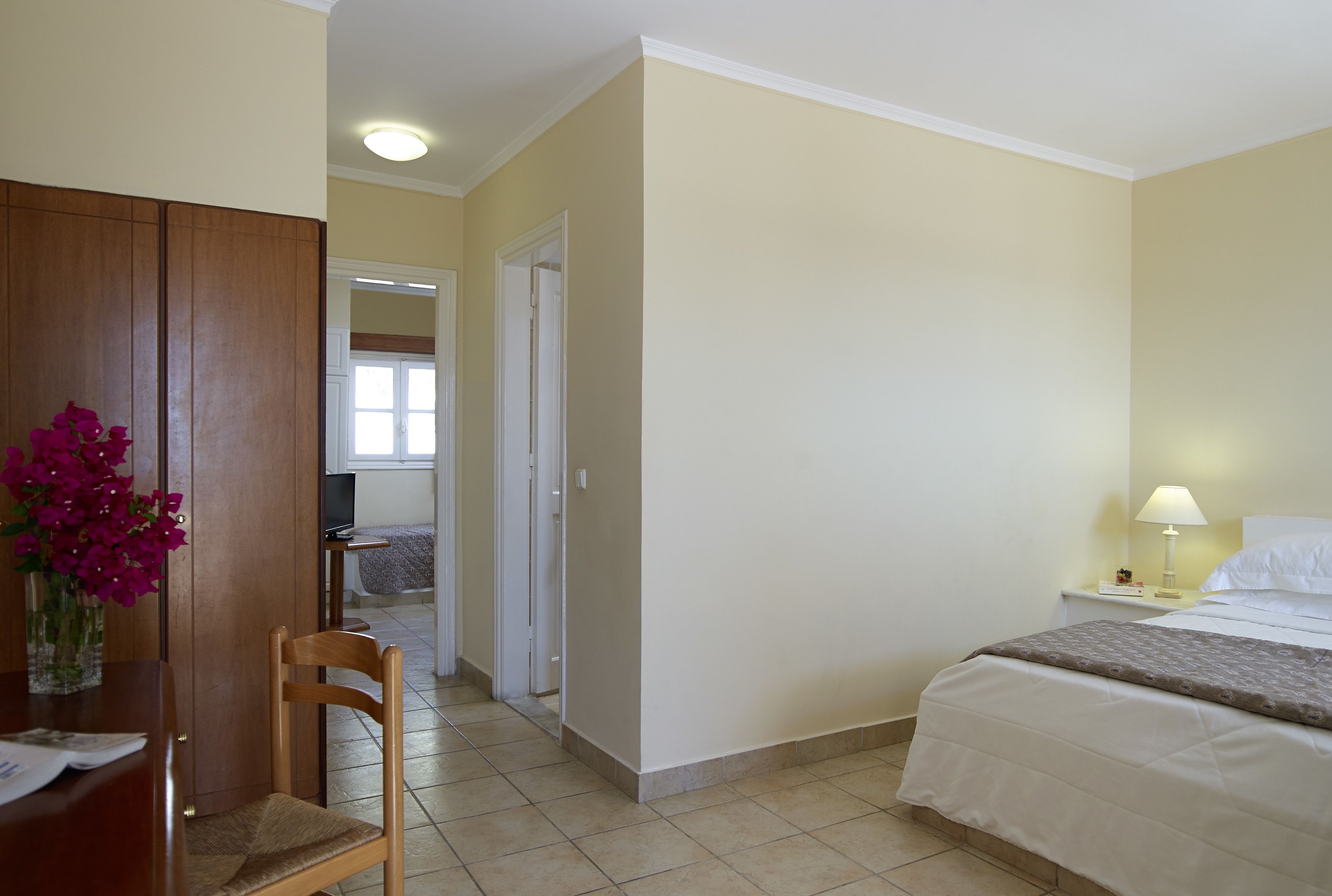 A hotel room with a bed, bedside table, lamp, and a wooden chair.