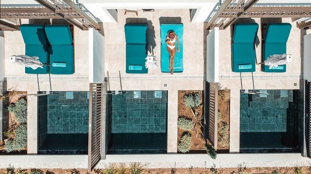 Un área de piscina exterior moderna con numerosas tumbonas y una persona relajándose en una de ellas.