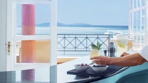 Une chambre avec vue sur la mer, une table avec une boisson et des fruits, et une balustrade de balcon.