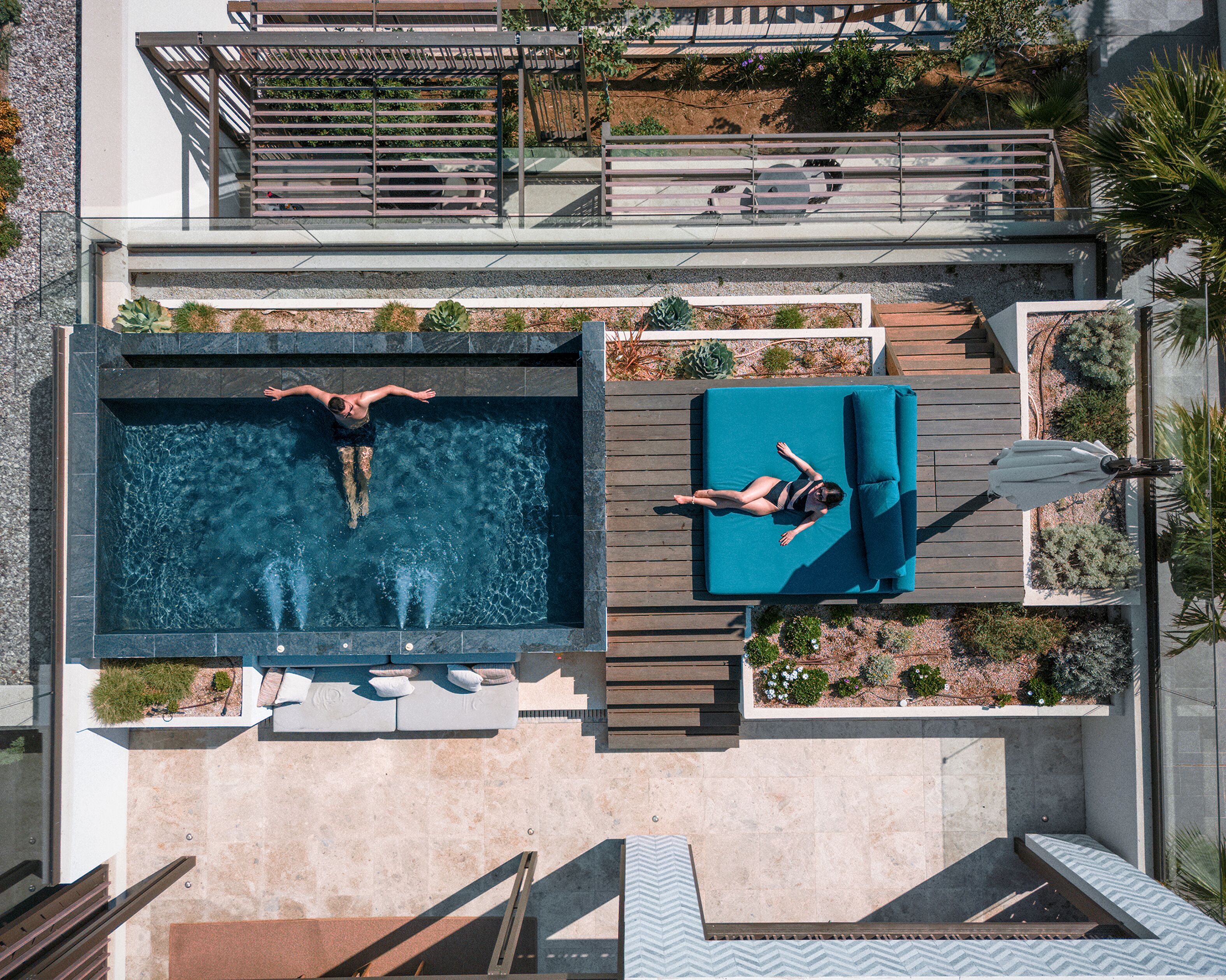 Una piscina en la azotea con dos personas nadando, una tumbona y un pequeño jardín.