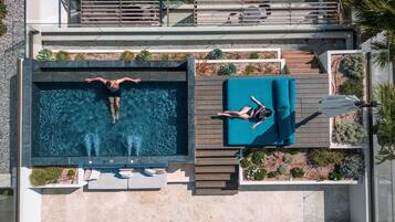 Una piscina en la azotea con dos personas nadando, una tumbona y un pequeño jardín.