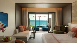 Une chambre d’hôtel avec un lit, un canapé, une chaise, une petite table et une vue sur l’océan.