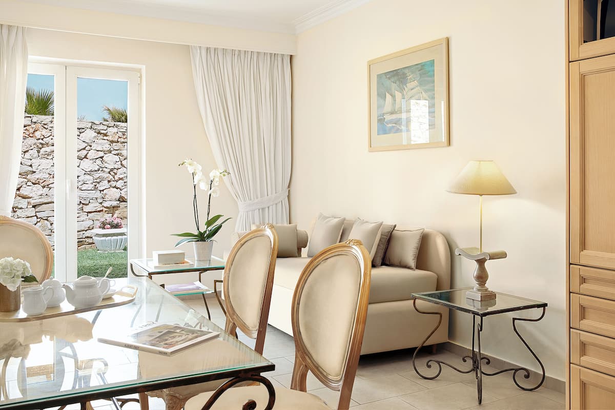 A well-lit living room with a glass table, chairs, a sofa, a lamp, and a painting on the wall.