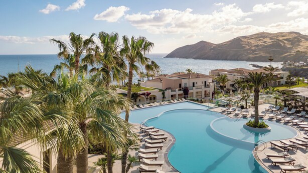 A resort with a large pool, palm trees, and a view of the sea and mountains.