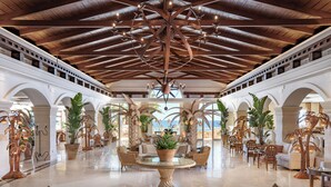 A spacious lobby with high ceilings, a central seating area, and large windows overlooking the sea.
