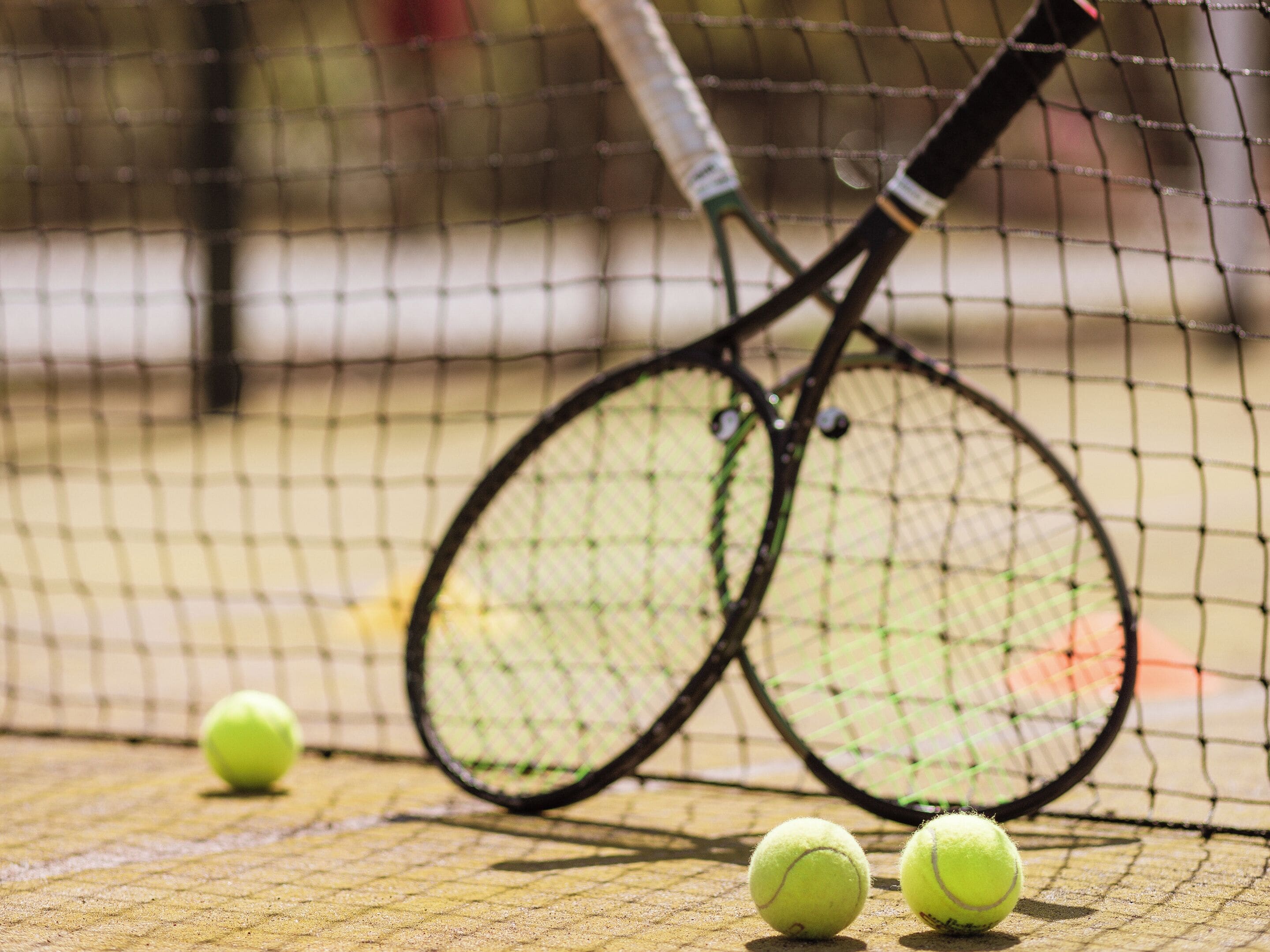 A tennis court with a net, two tennis rackets, and three tennis balls.