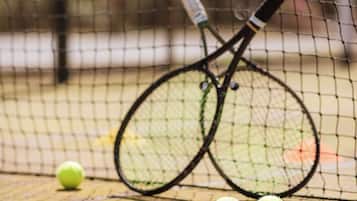 Una cancha de tenis con una red, dos raquetas y tres pelotas.