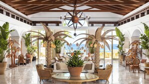 A spacious lobby with high ceilings, large windows, and tropical plants.