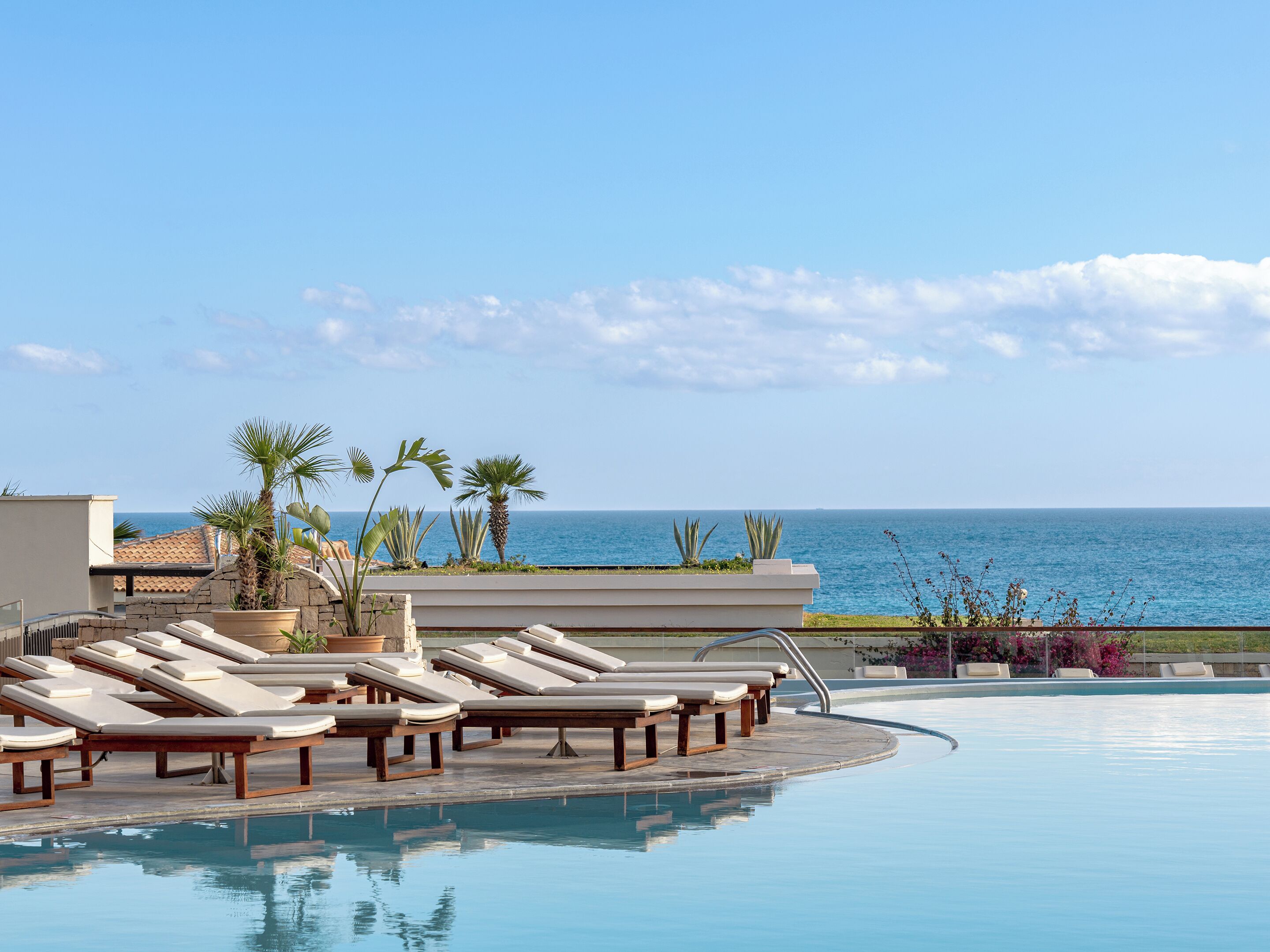 A poolside area with lounge chairs and a view of the ocean.