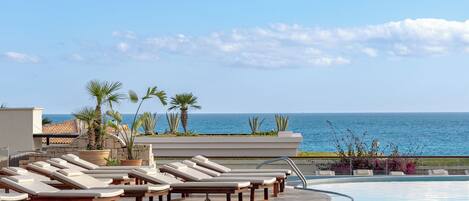 A poolside area with lounge chairs and a view of the ocean.