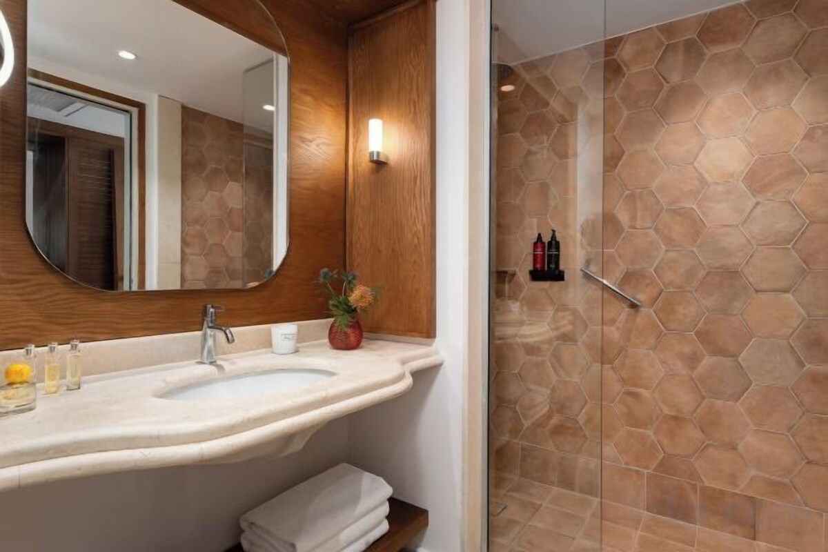 A bathroom with a double sink, a mirror, and a shower with hexagonal tiles.
