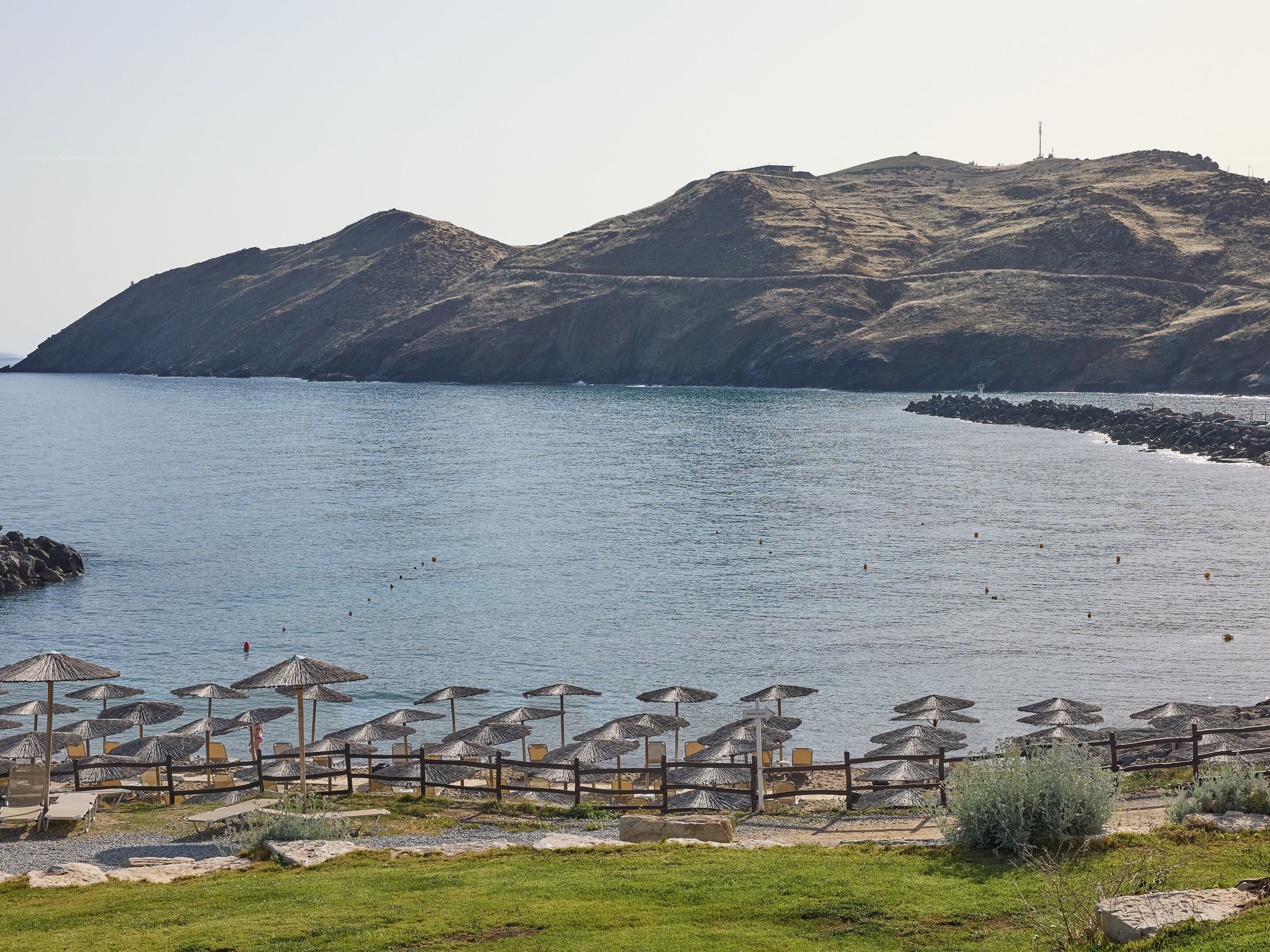 Une plage avec des parasols et des chaises, un rivage rocheux et des montagnes en arrière-plan.