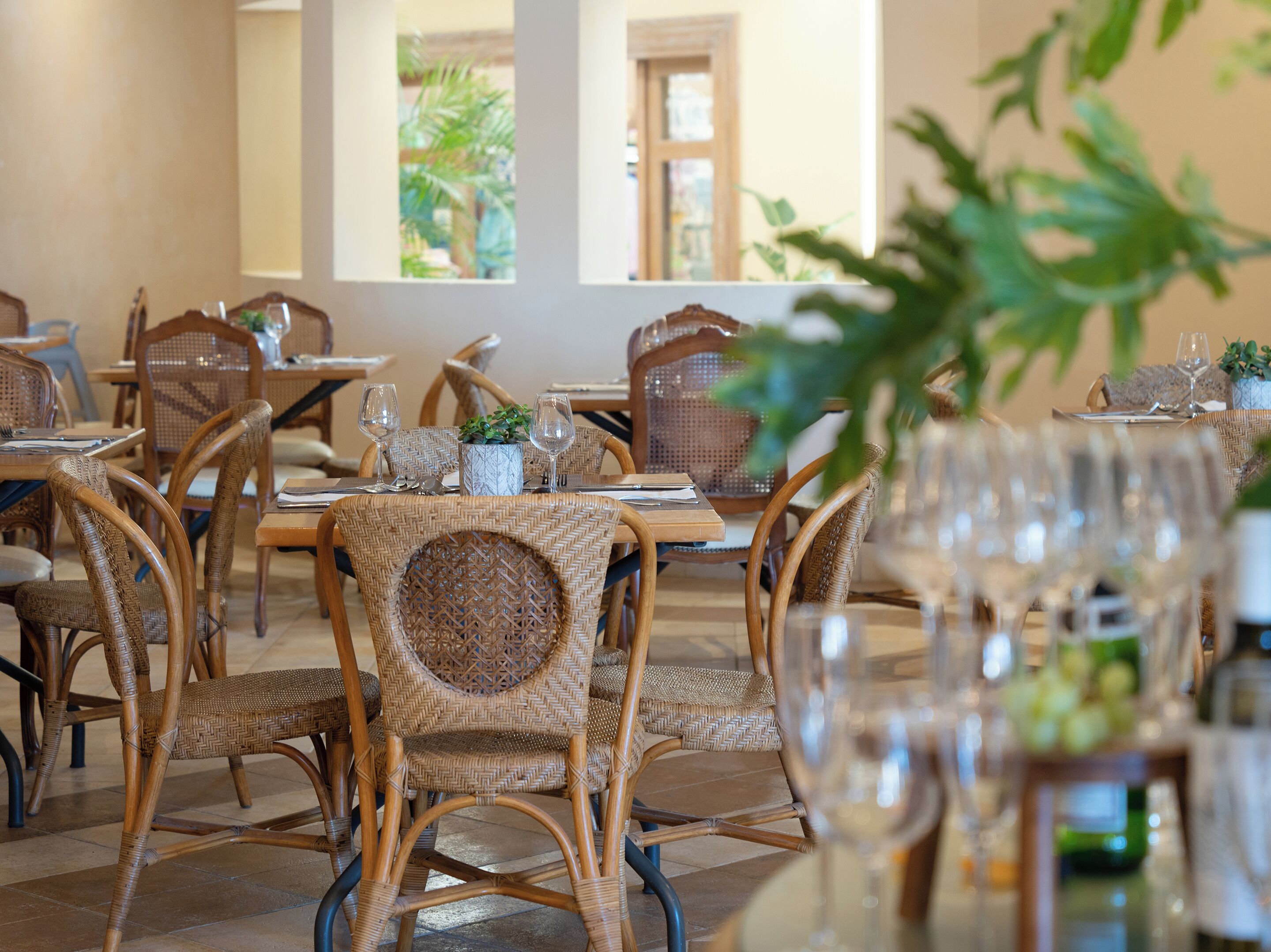 A dining area with wicker chairs and tables, each set with wine glasses and cutlery.