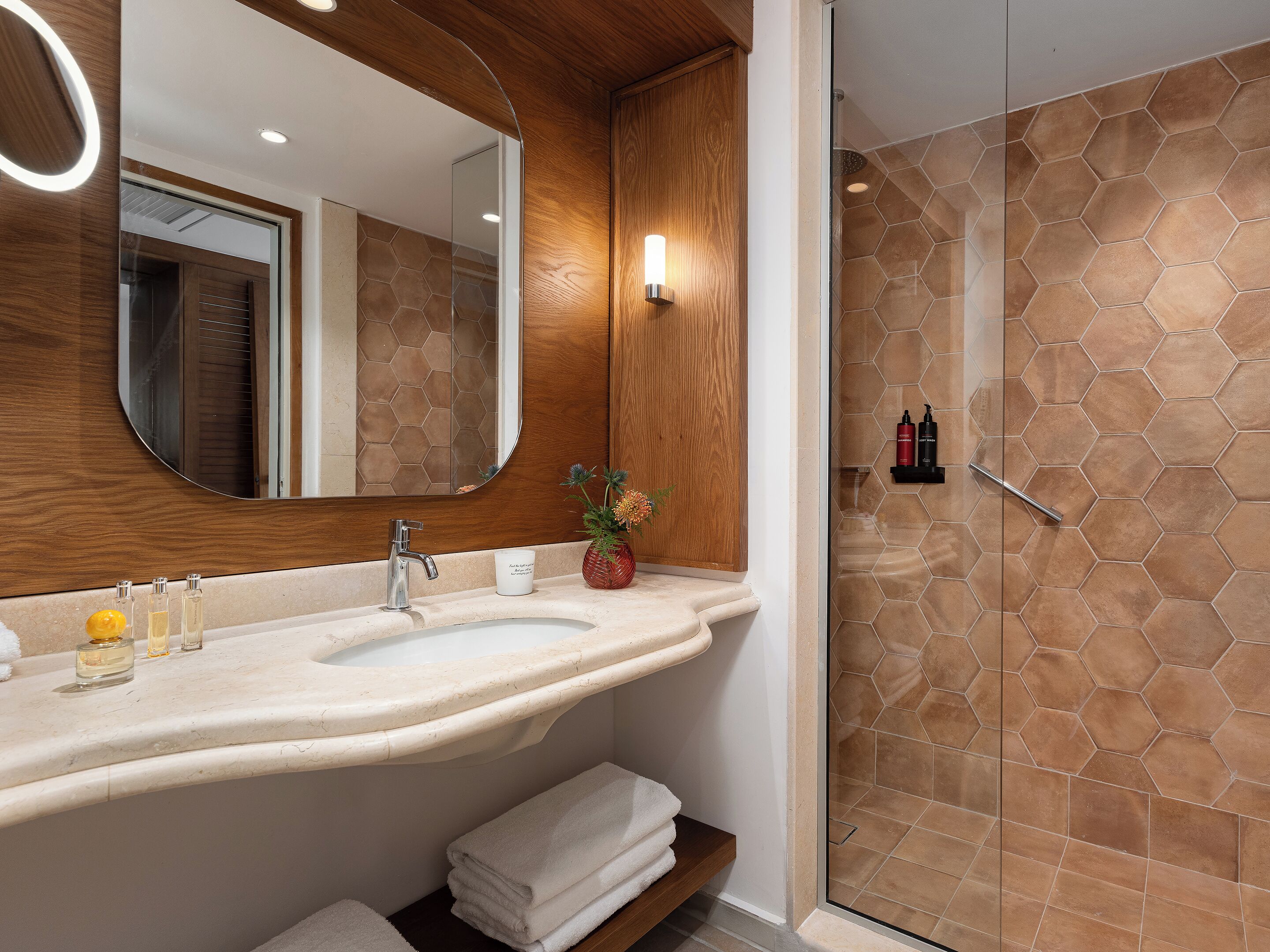 A bathroom with a wooden vanity, a large mirror, a sink, and a shower with hexagonal tiles.