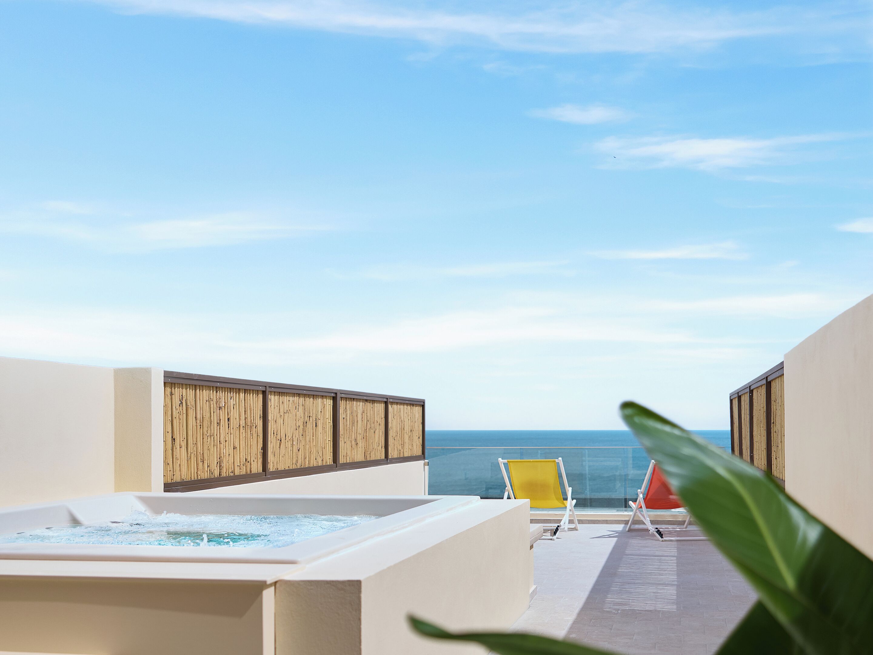 A rooftop terrace with a hot tub, two lounge chairs, and a view of the ocean.