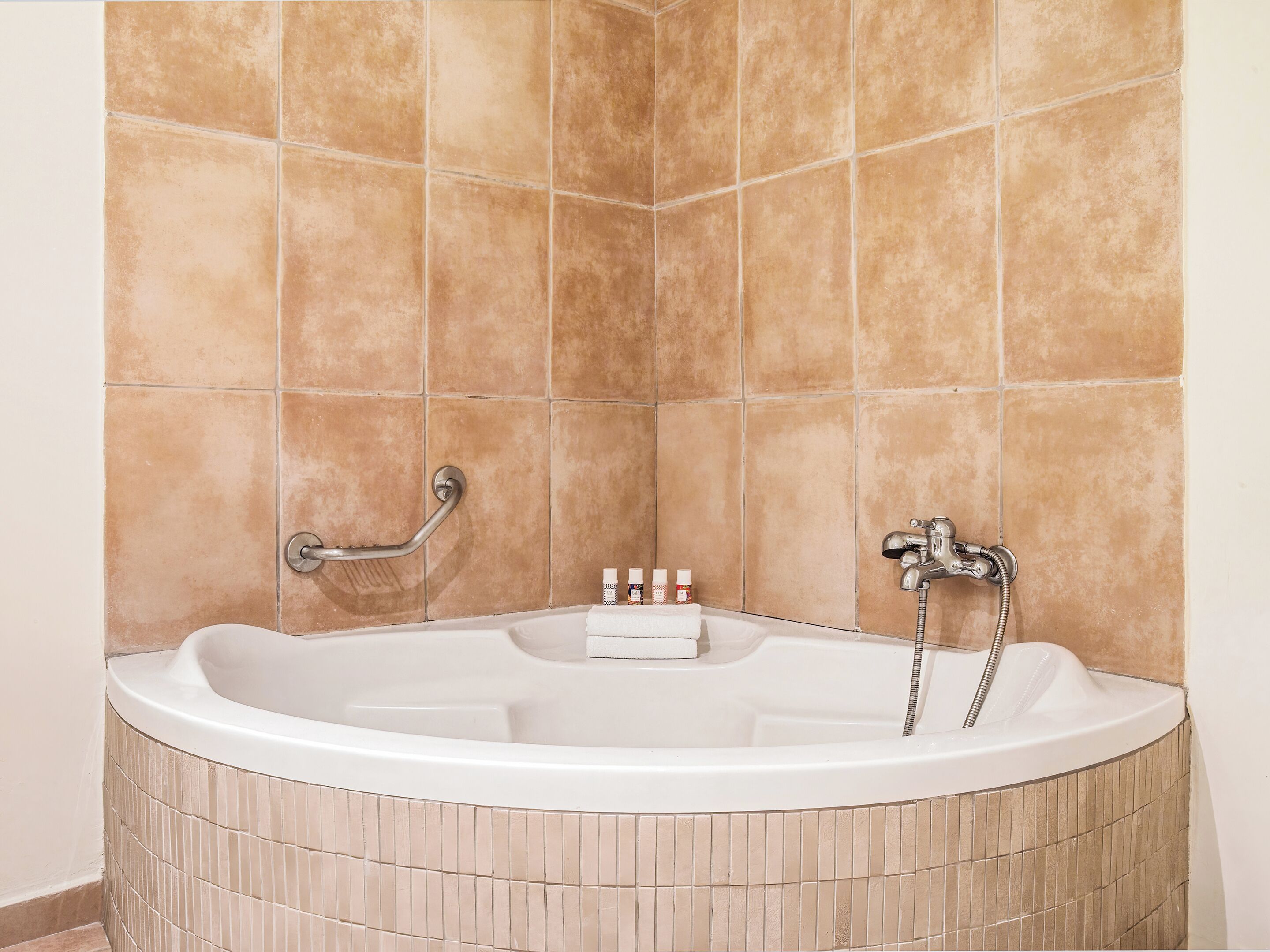 Une baignoire équipée d’une barre d’appui, d’un pommeau de douche et d’une bouteille de shampoing posée sur le bord.