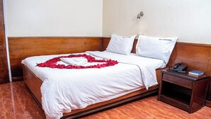 A hotel room with a bed, a wooden headboard, a bedside table with a phone and a book, and a wall-mounted light. - Hotel Ambassadeur (Nairobi)