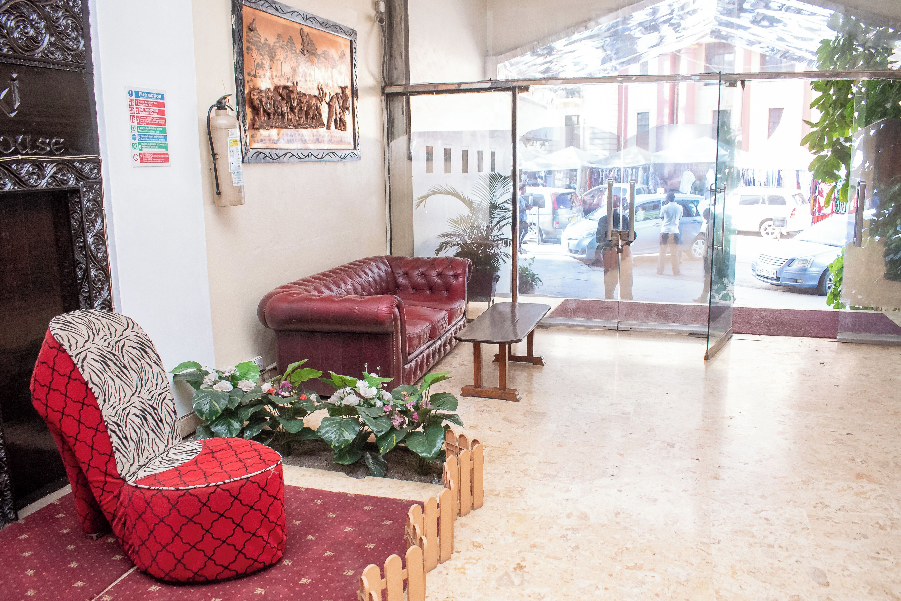 Um hall com um sofá de couro vermelho, uma poltrona estampada, uma mesinha e um vaso de planta.