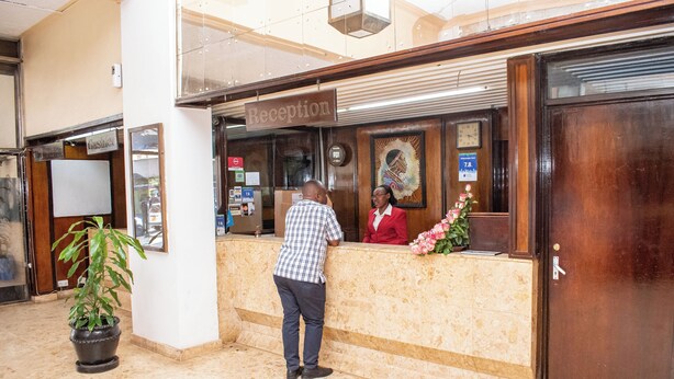 A reception area with a reception desk, a clock, and a potted plant. - Hotel Ambassadeur (Nairobi)