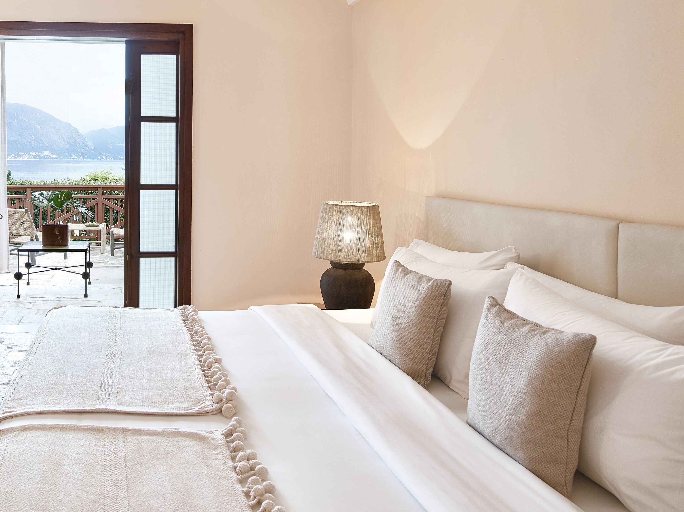 A bedroom with a bed, a lamp, and a view of the outdoors.