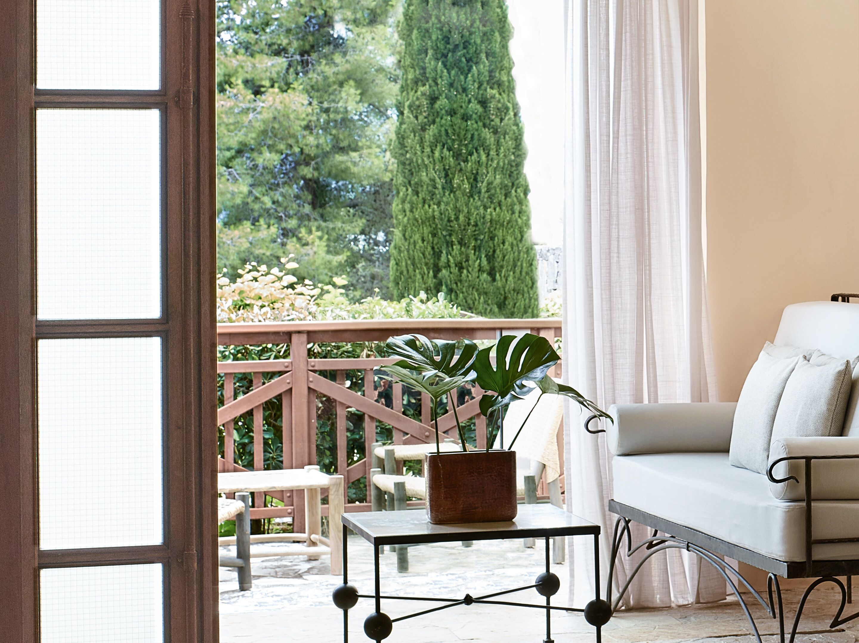 Une pièce donnant sur un jardin, avec un canapé blanc, une petite table sur laquelle est posée une plante en pot et une rambarde en bois.