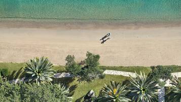 Vue aérienne d’une plage aux eaux turquoise et limpides, bordée d’un rivage sablonneux et de palmiers.