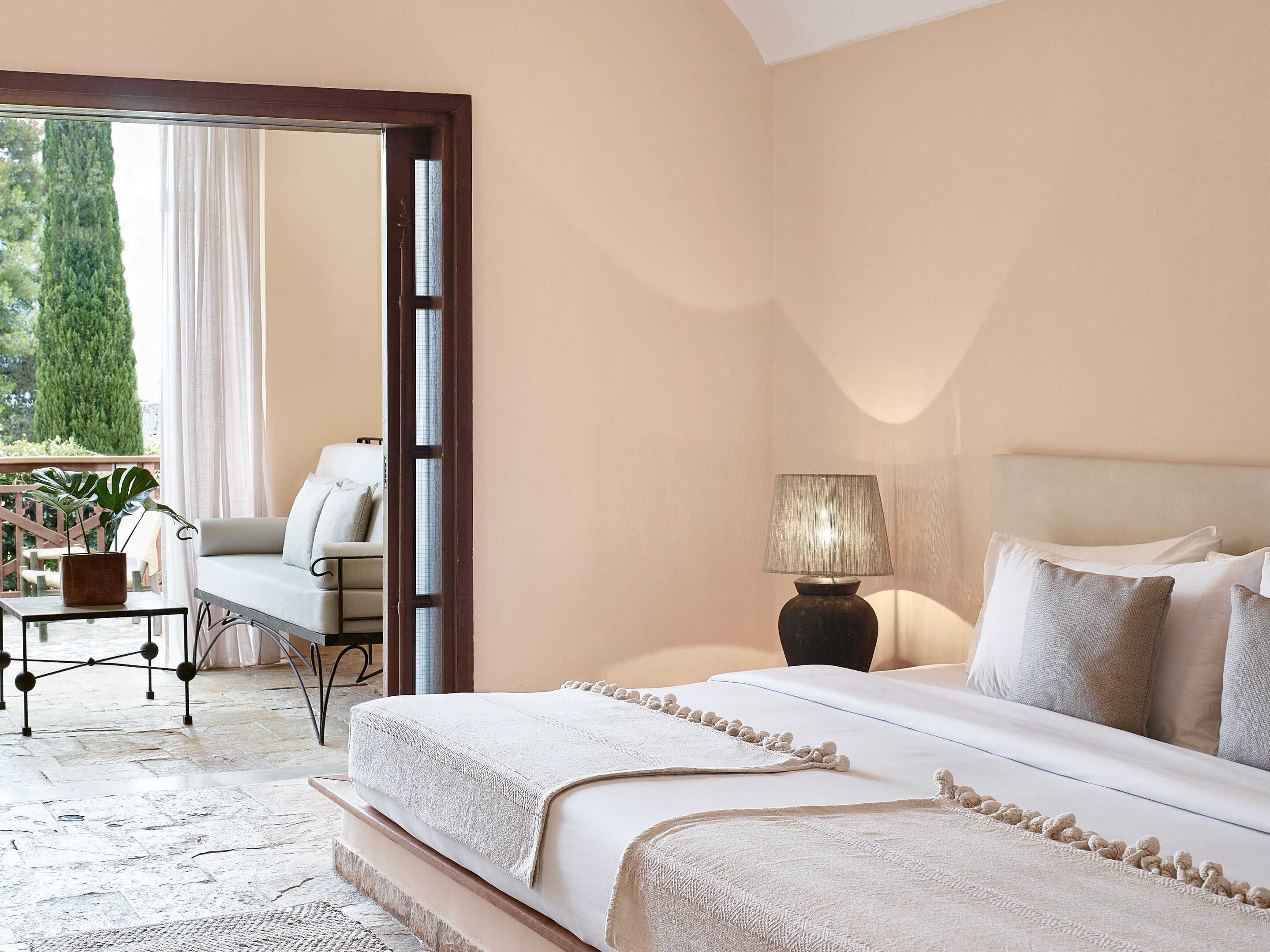 A bedroom with a bed, a nightstand, a lamp, and a view of the outdoors through a door.