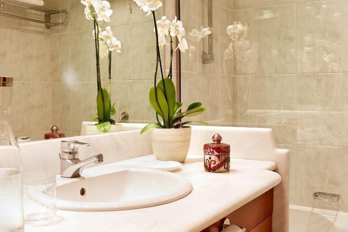 A bathroom with a white sink, a mirror, and two potted plants.