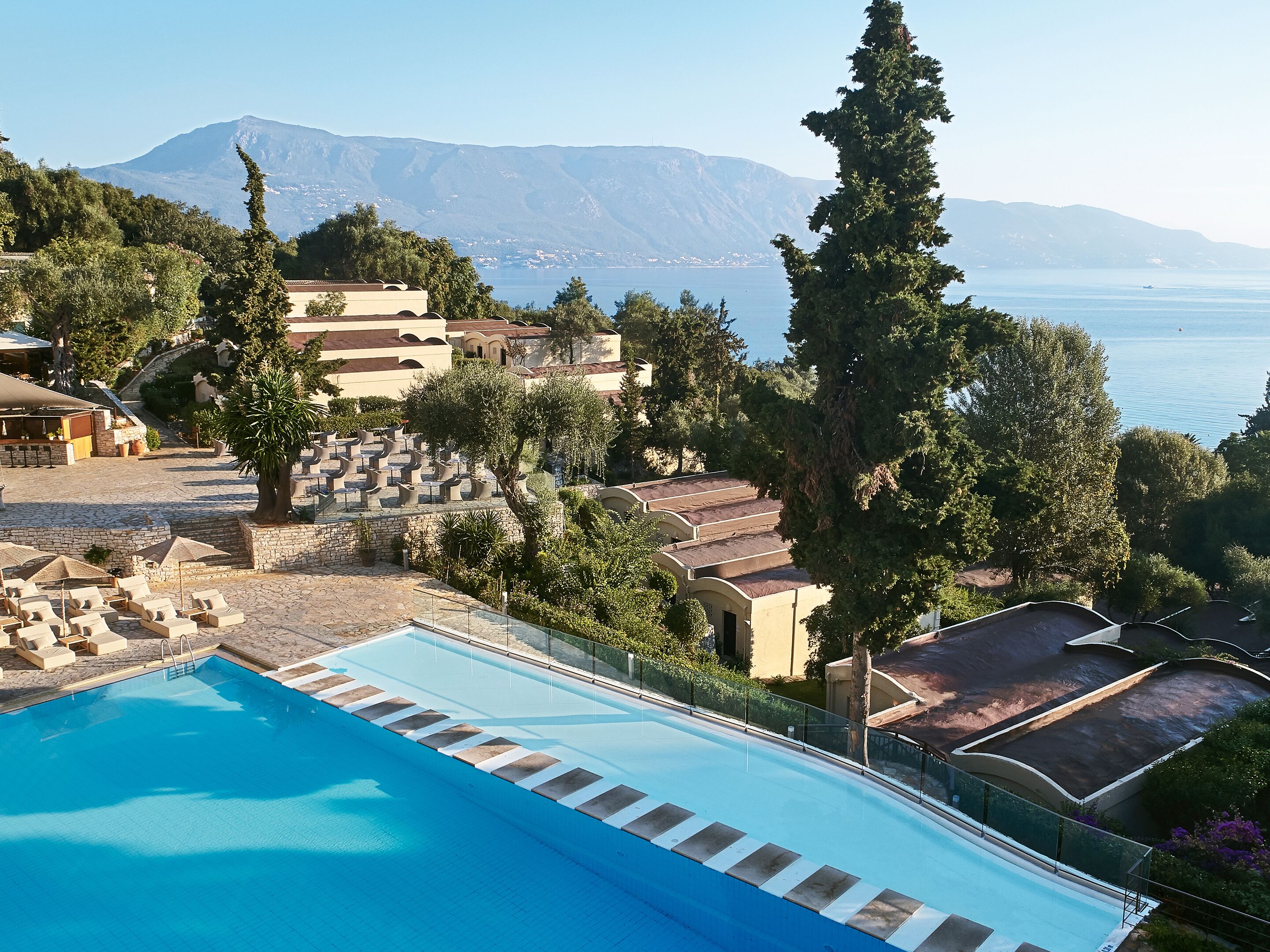 A swimming pool with lounge chairs, a stone pathway, and a view of the sea and mountains.