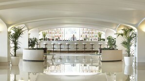 Zona bar con soffitto alto, pavimento lucido e un barista al bancone.