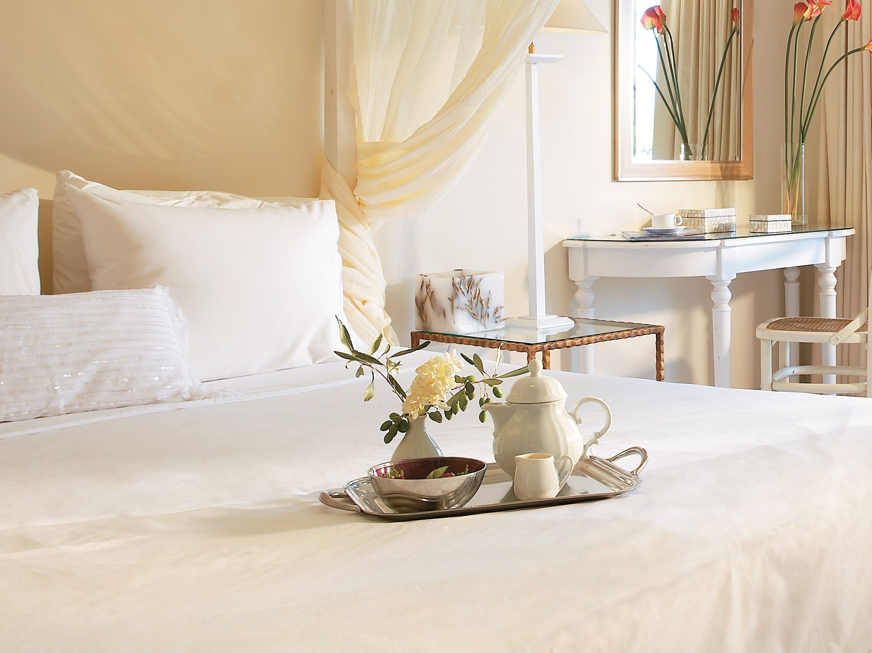 Ein ordentlich bezogenes Bett mit einem Frühstücksbrettchen, eine weiße Kommode und ein Sessel in einem Hotelzimmer.