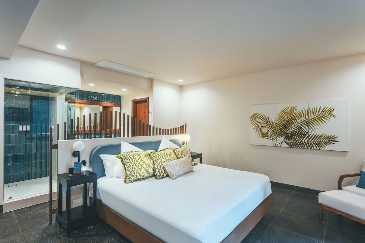 Une chambre d’hôtel moderne dotée d’un grand lit, d’une table de chevet, d’un coin salon et d’une salle de bain avec une douche en verre.