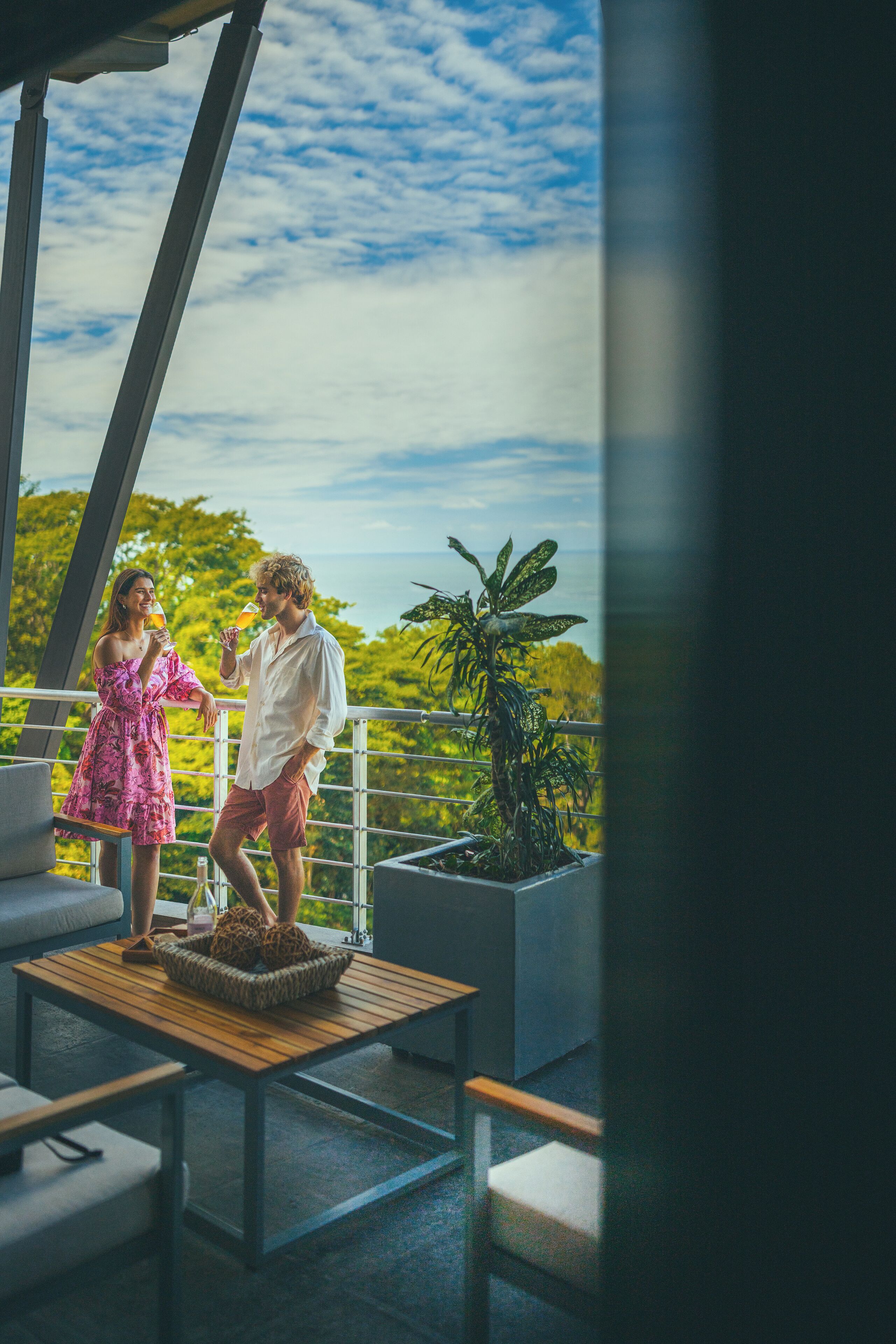 A couple on a balcony with a view of greenery and a clear sky.