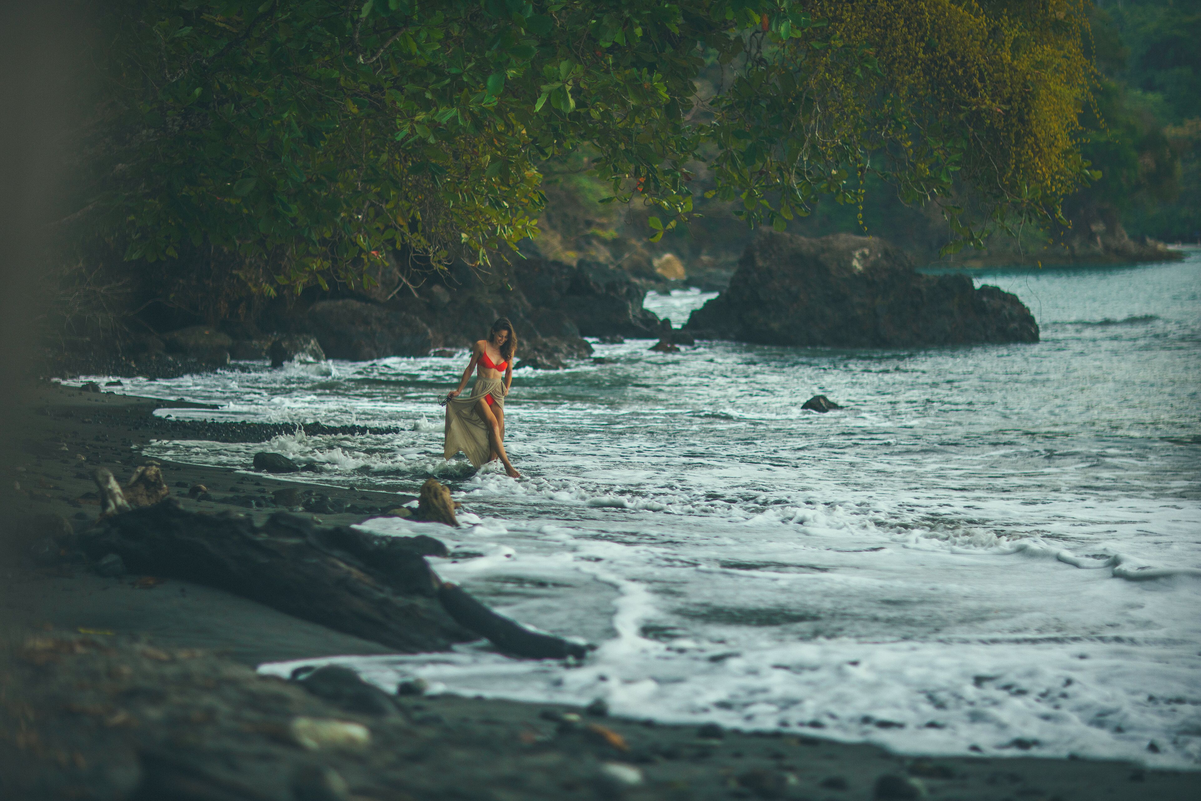 A beach with rocky terrain and a person in a swimsuit.