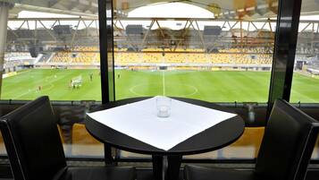 A table with a glass and a candle, facing a stadium with yellow seats and a green field.