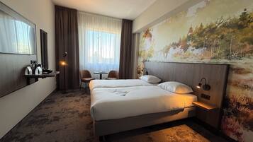 Une chambre d’hôtel avec deux lits, un bureau avec une chaise, une petite table et une grande fenêtre avec des rideaux.