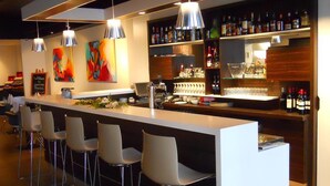 Zona de bar moderna con una barra larga, varios taburetes y lámparas colgantes.