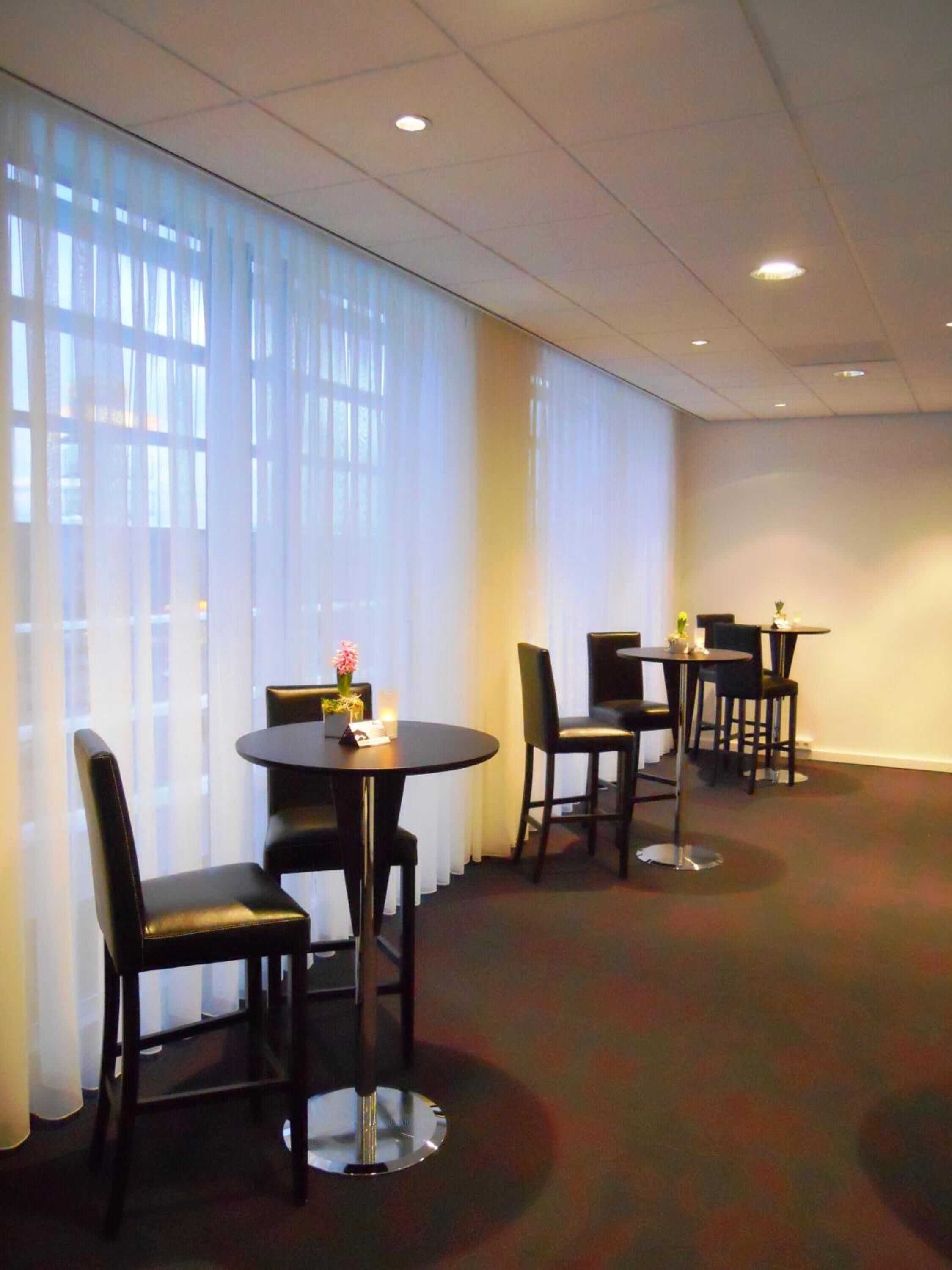 Une chambre d’hôtel avec une grande fenêtre, une table ronde avec des chaises et une table plus petite, également avec des chaises.