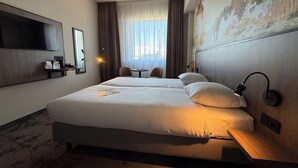 Habitación de hotel con dos camas, un televisor de pantalla plana, una mesita y una lámpara de pared.