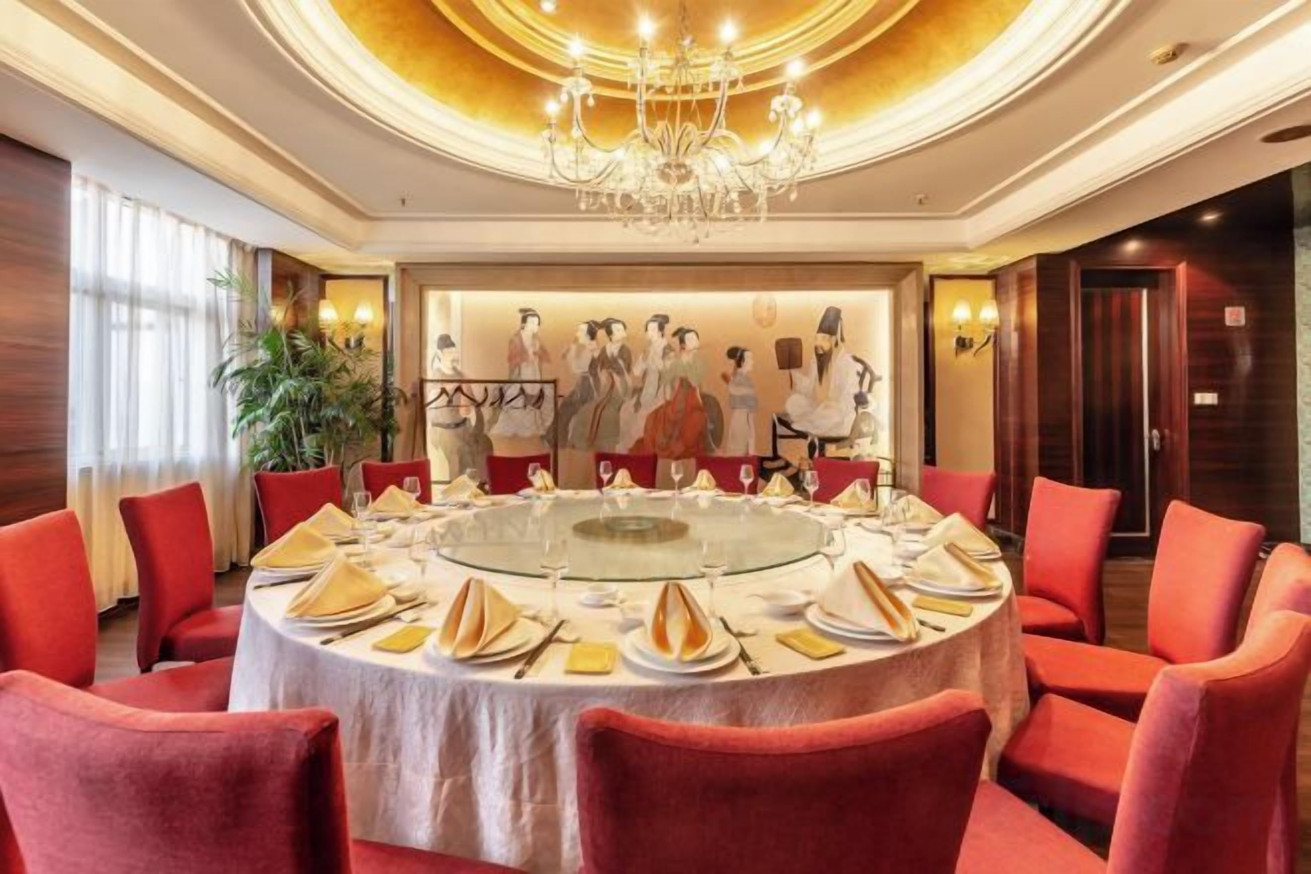 A round table with a glass top surrounded by red upholstered chairs, set for a meal.