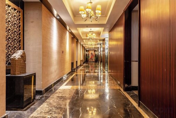Un pasillo de hotel con suelo de mármol, paredes de madera y una araña.