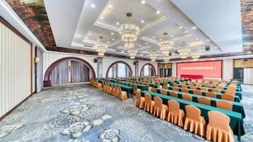 Un salón de conferencias con hileras de sillas, un escenario y una gran pantalla.