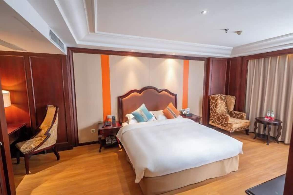 Habitación de hotel con una cama grande, una mesita de noche de madera, una silla y un escritorio.