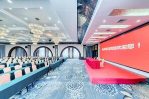 Un salón de conferencias con filas de sillas, un escenario con alfombra roja y una pantalla grande con texto.