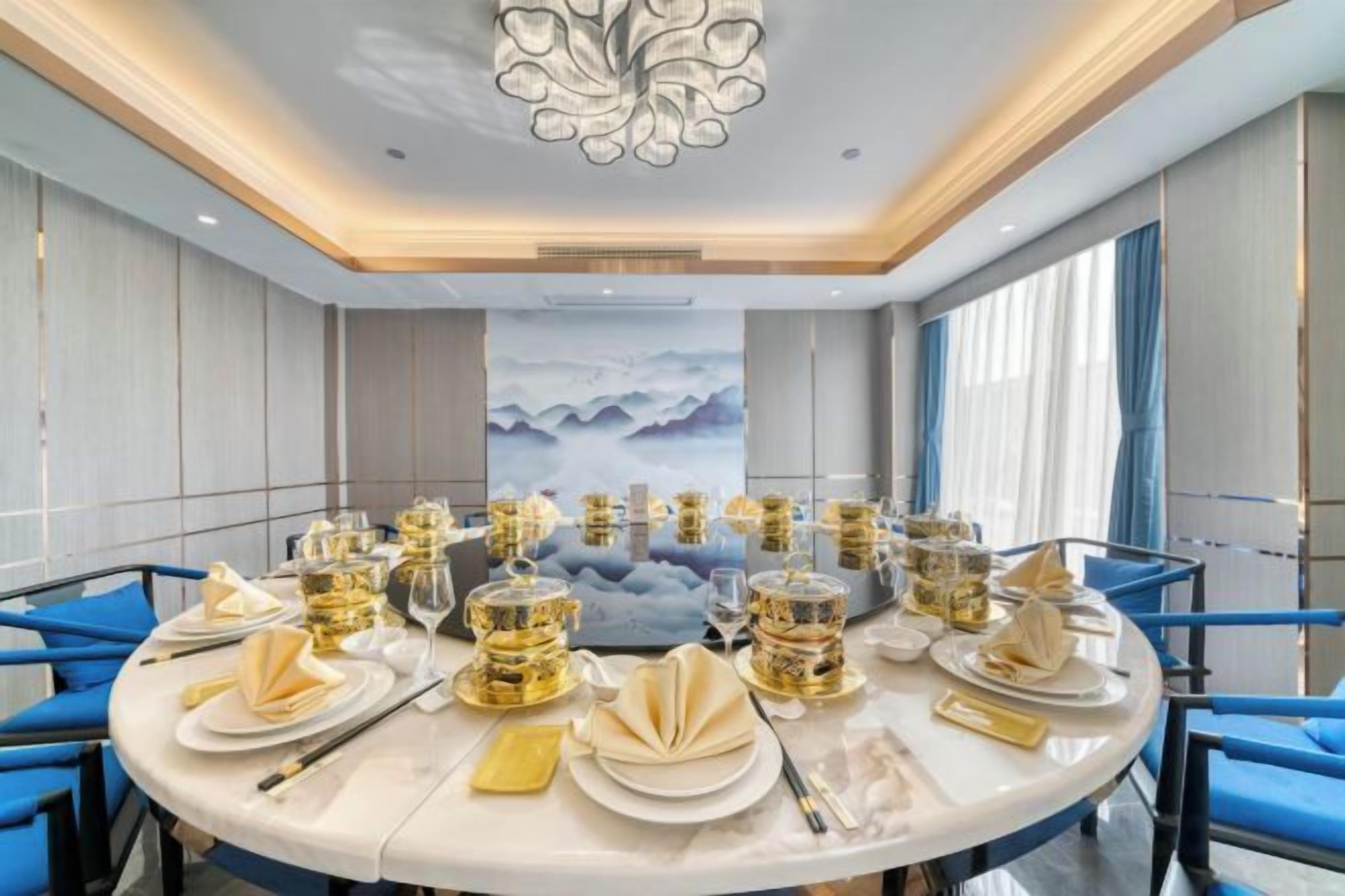 Taula rodona amb plats preparats per a dinar, voltada per cadirees, a una habitació amb un disseny modern i un gran finestral.