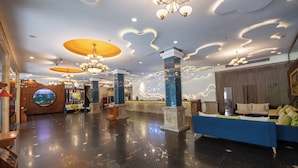 A hotel lobby with a reception desk, seating area, and a large mirror reflecting the interior. - Romance Hotel (Hue)