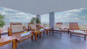 A rooftop terrace with wooden lounge chairs, a small table with a drink, and a view of the cityscape. - Romance Hotel (Hue)