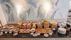 A buffet with various dishes and a large abstract painting in the background. - Romance Hotel (Hue)